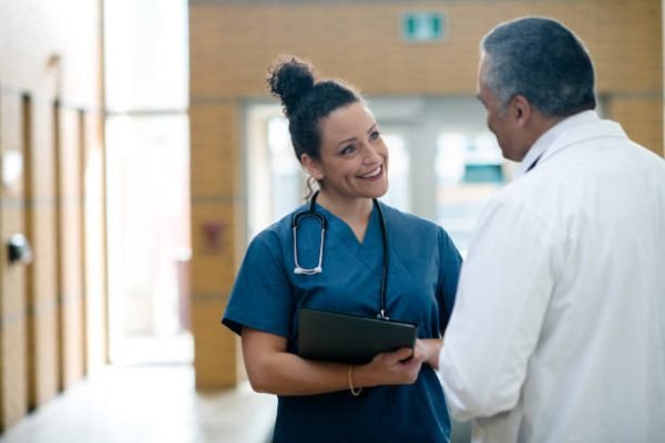 Two (2) doctors converse in a hallway as they have limited time to speak to each other.
